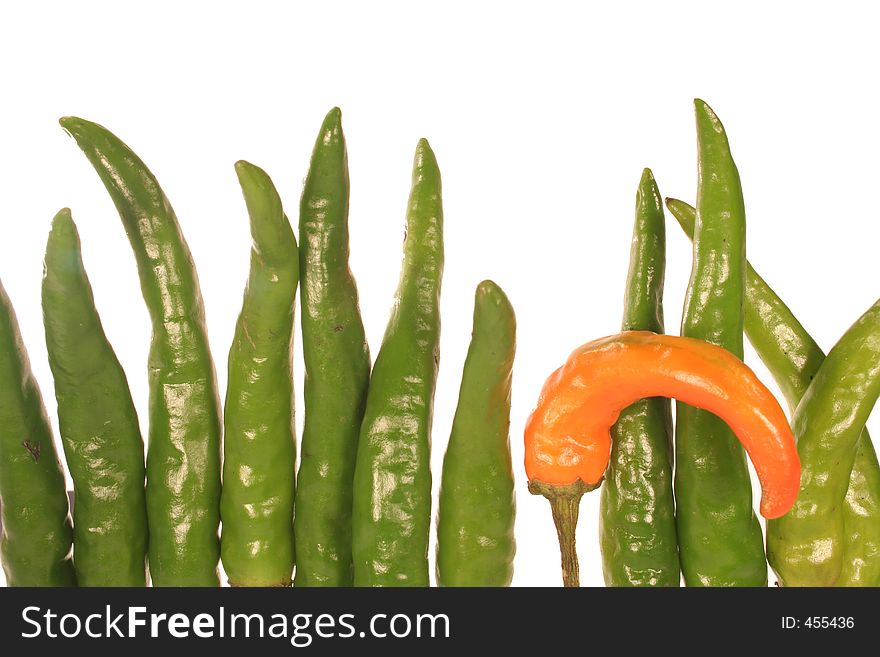 A wall of green chilis with one orange chili that is slightly bent. A wall of green chilis with one orange chili that is slightly bent