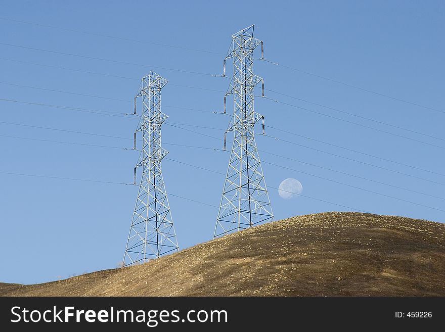 Hight voltage lines are held aloft by giant power towers, as the moon sets in the background. The hills appear scorched by a recent brush fire. Hight voltage lines are held aloft by giant power towers, as the moon sets in the background. The hills appear scorched by a recent brush fire.