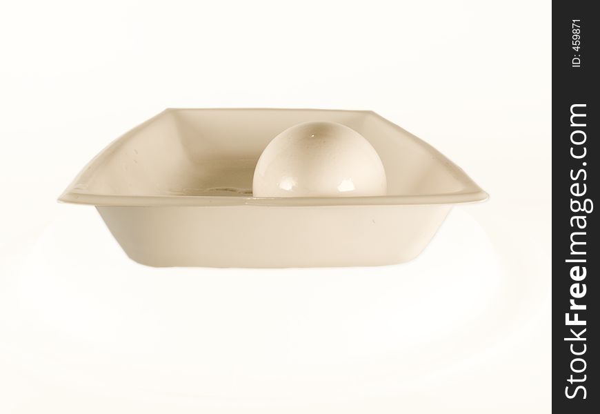 An isolated egg surrounded by a white background sits in a dish. After its shell is compromised, it will be ready to be served for breakfast. An isolated egg surrounded by a white background sits in a dish. After its shell is compromised, it will be ready to be served for breakfast.