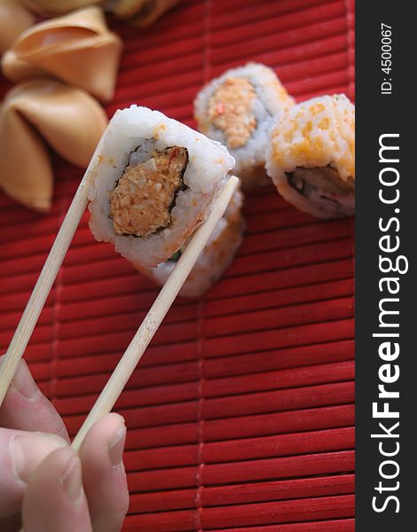 California rolls being picked up with chopsticks on a red mat. California rolls being picked up with chopsticks on a red mat