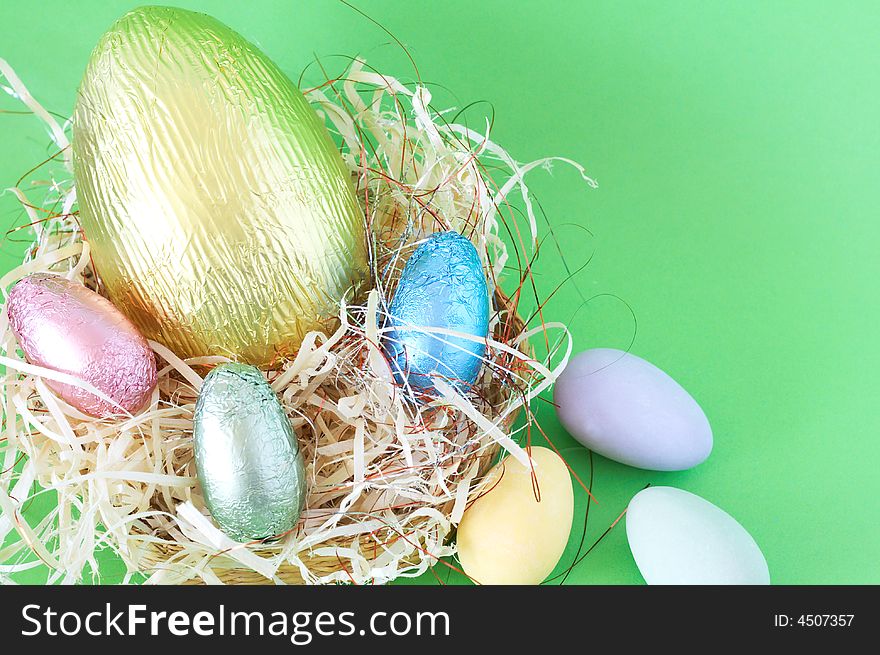 Chocolate Easter eggs in straw on green background