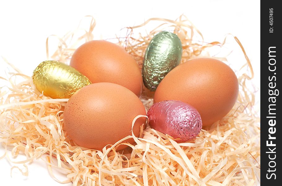 Real Easter and colorful chocolate eggs in straw on white background. Real Easter and colorful chocolate eggs in straw on white background