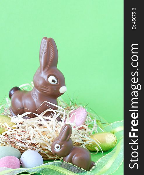 Two chocolate Easter bunnies with colorful chocolate eggs in straw