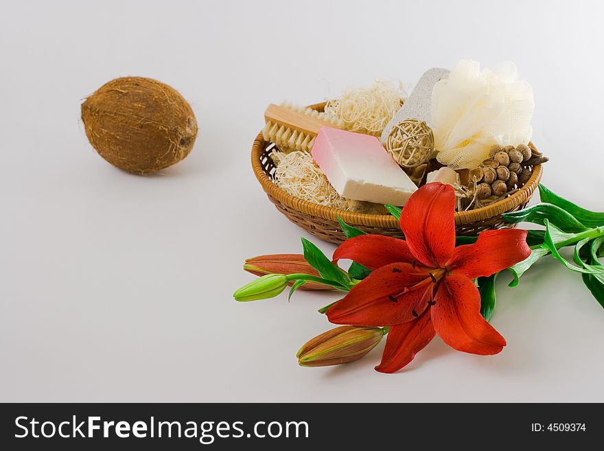 Personal care items and decorations in a basket, a coconut and a red lily isolated on white background.