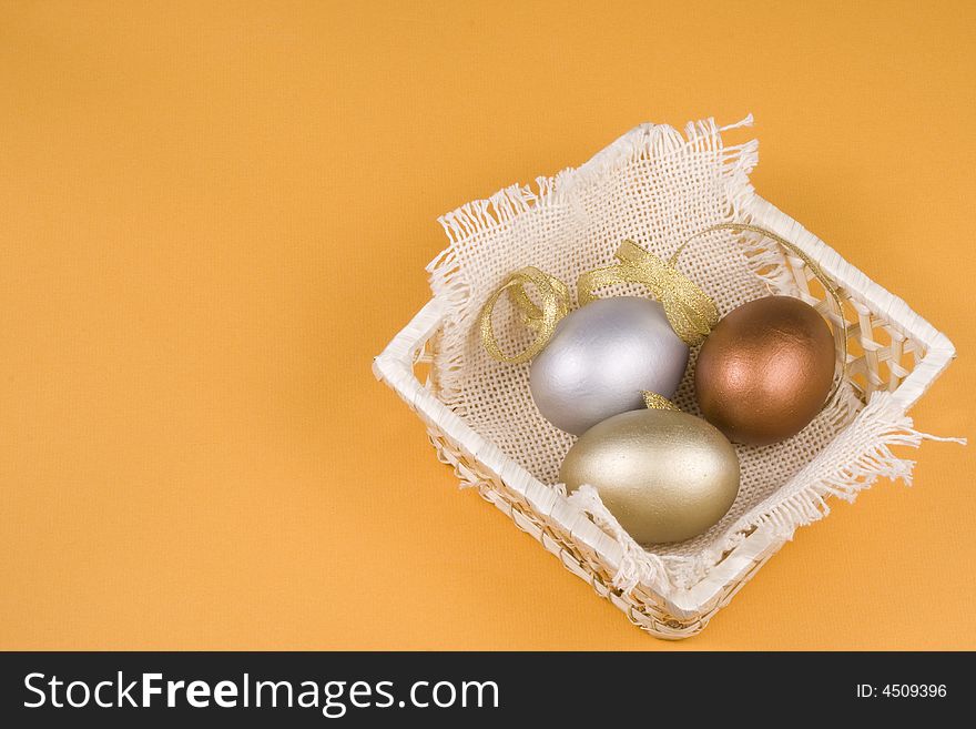 Gold, silver and bronze eggs in a basket on a yellow background.