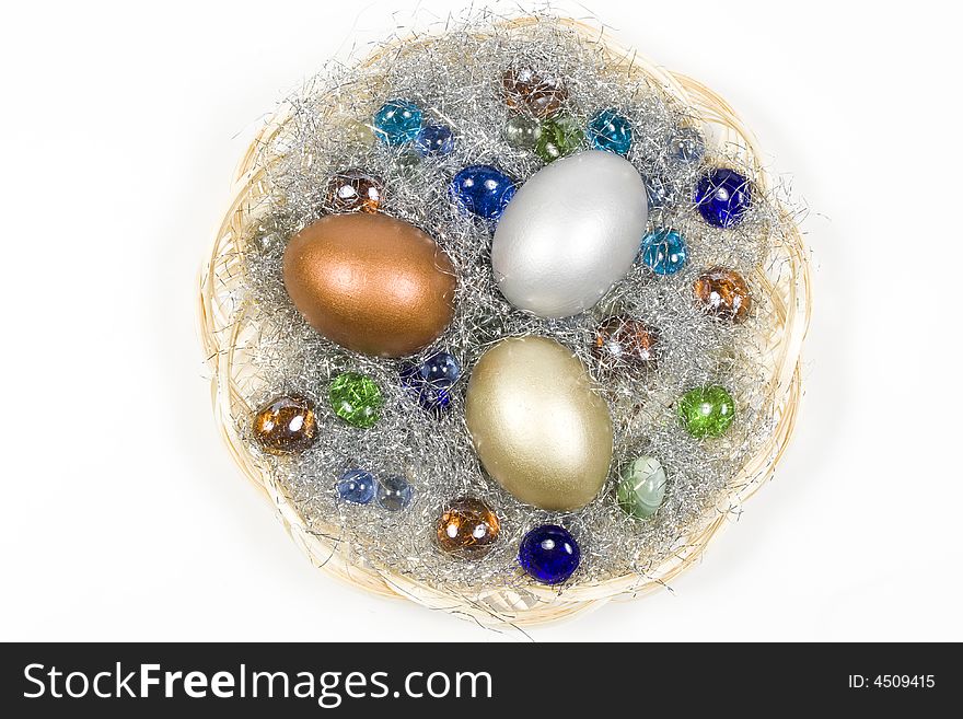 Gold, silver and bronze eggs in a basket with a glass stones. Isolated on a white background.