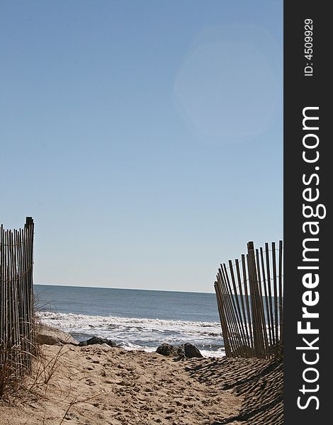 Path to the beach lined with a fence on a sunny blue sky day. Path to the beach lined with a fence on a sunny blue sky day.