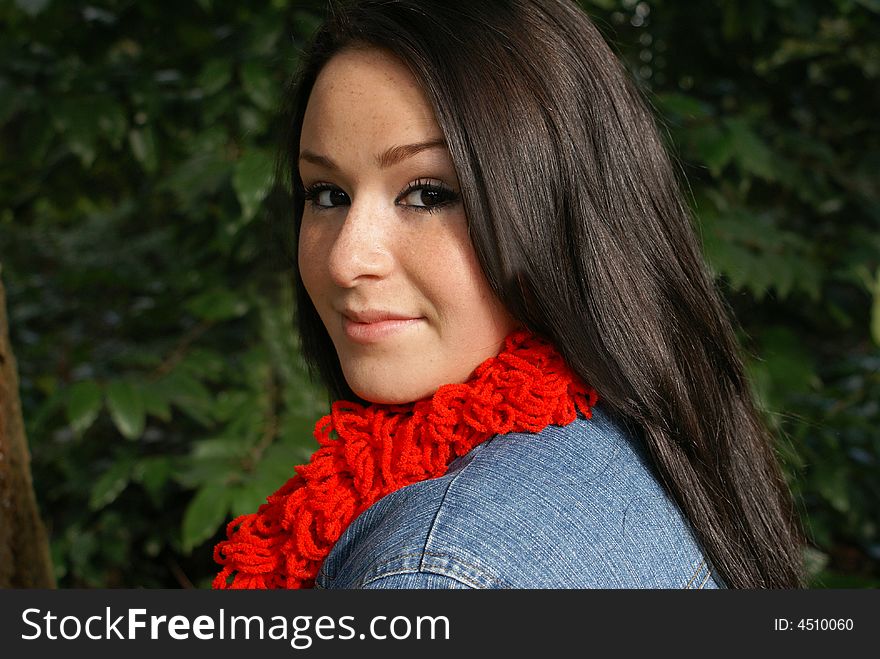 Close-up of girl wearing red scarf and coy expression isolated against wooded background. Close-up of girl wearing red scarf and coy expression isolated against wooded background