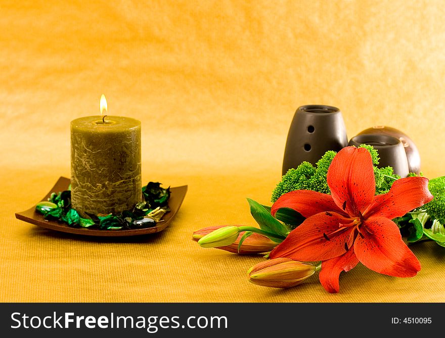 Red lily, green scented candle and black oil burner on golden background. Red lily, green scented candle and black oil burner on golden background.