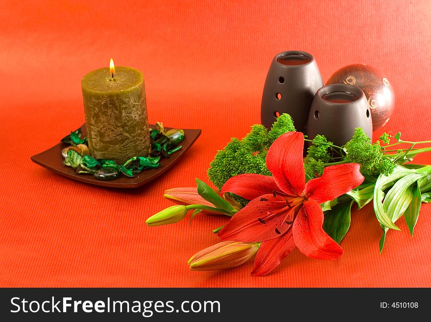 Red lily, red scented candle and black oil burner on red background. Red lily, red scented candle and black oil burner on red background.