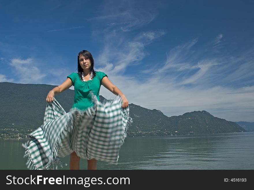 Woman extending a tablecloth for a picnic at the edge of a lake