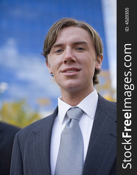 Close front view of single white businessman in suit in front of blue office building. Close front view of single white businessman in suit in front of blue office building