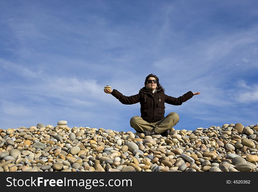 Young woman in lotus pose with round peebles in the hand - yoga and zen concept