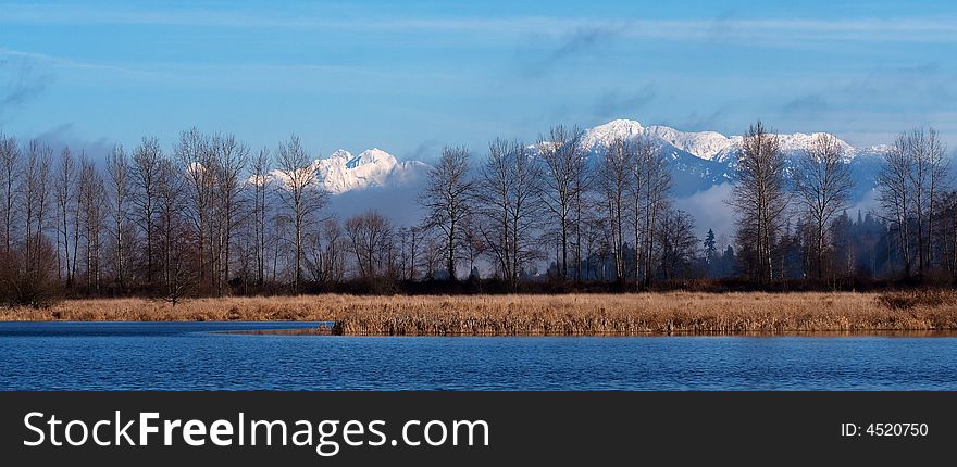 The Cascade Mountains in winter snow as seen across Shadow Lake at the Bob Heirman Wildlife Preserve in Snohomish, WA.