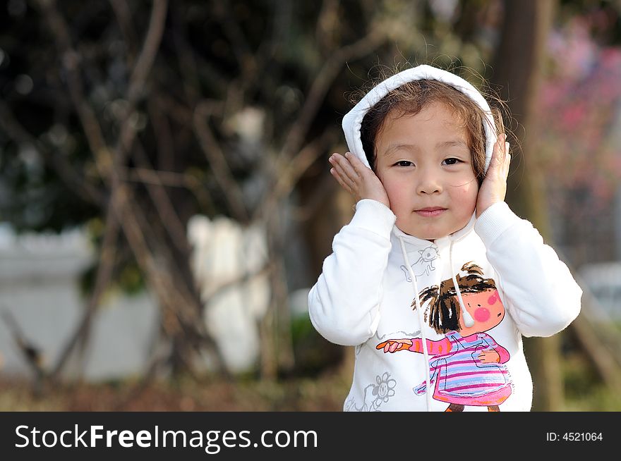 The cute little girl is touching her red face by her small hands.