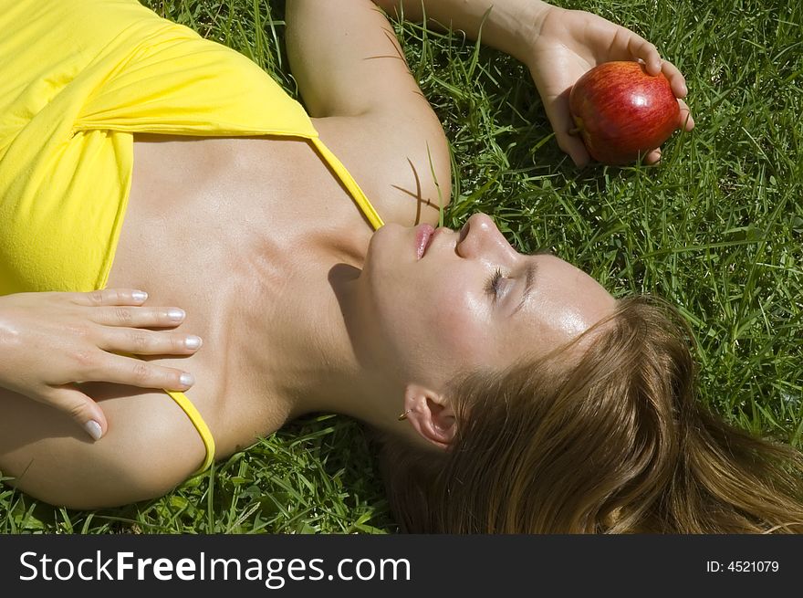 Young tanned woman resting on the grass with red apple. Young tanned woman resting on the grass with red apple