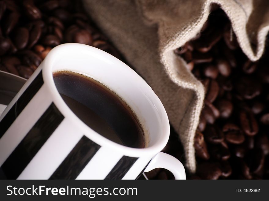 Some coffee beans and a jute sack behind a cup of black coffee. Some coffee beans and a jute sack behind a cup of black coffee