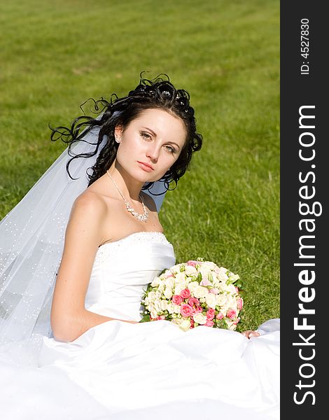 Beautiful bride with a flower bouquet on the green grass. Beautiful bride with a flower bouquet on the green grass
