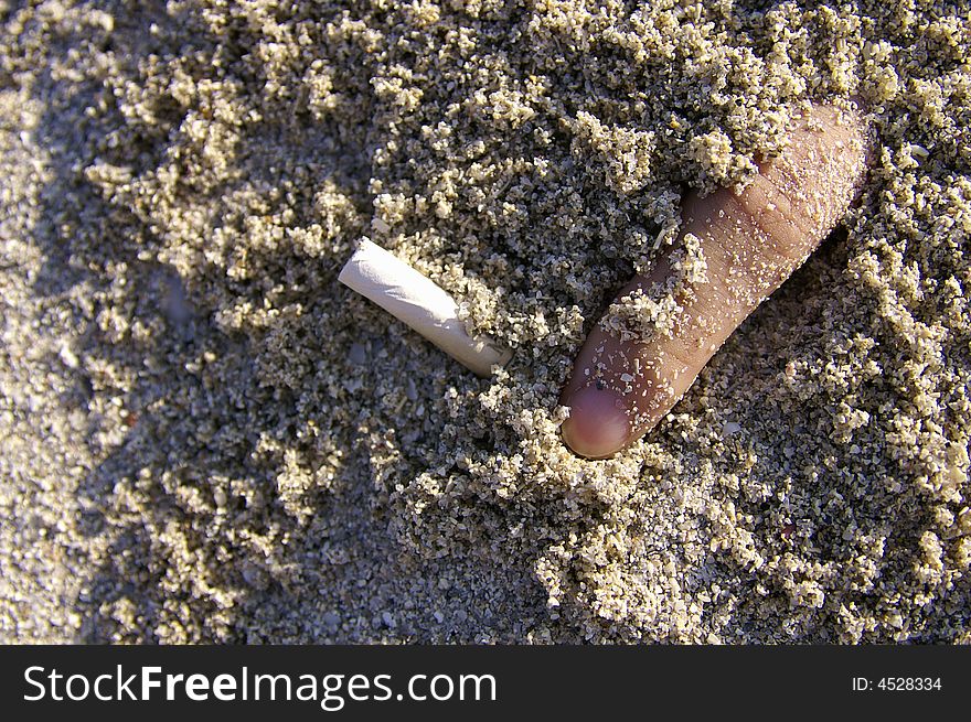 Finger with cigarette half buried in the sands. Finger with cigarette half buried in the sands