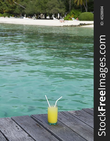 Drink in a glass with 2 straws with a beach in the background. Drink in a glass with 2 straws with a beach in the background.