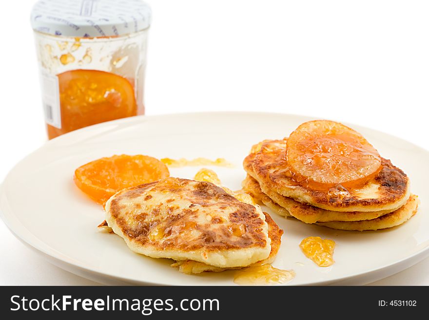 Small 
cottage pancakes with some orange jam, jam jar in background, isolated on white. Small 
cottage pancakes with some orange jam, jam jar in background, isolated on white