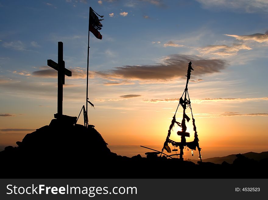 Top of mountain on sunrise on which the flag, a pyramid and a cross are located