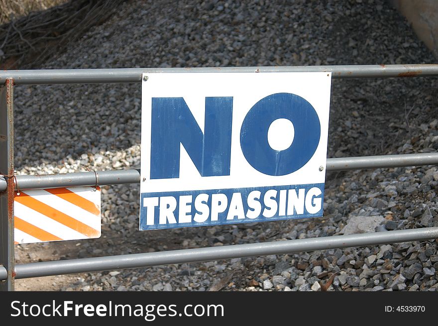 A blue no trespassing sign on a metal fence post