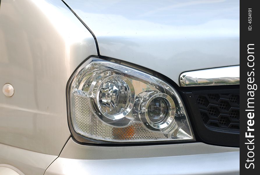 The left headlight of a microbus,grey silver vehicle. The left headlight of a microbus,grey silver vehicle