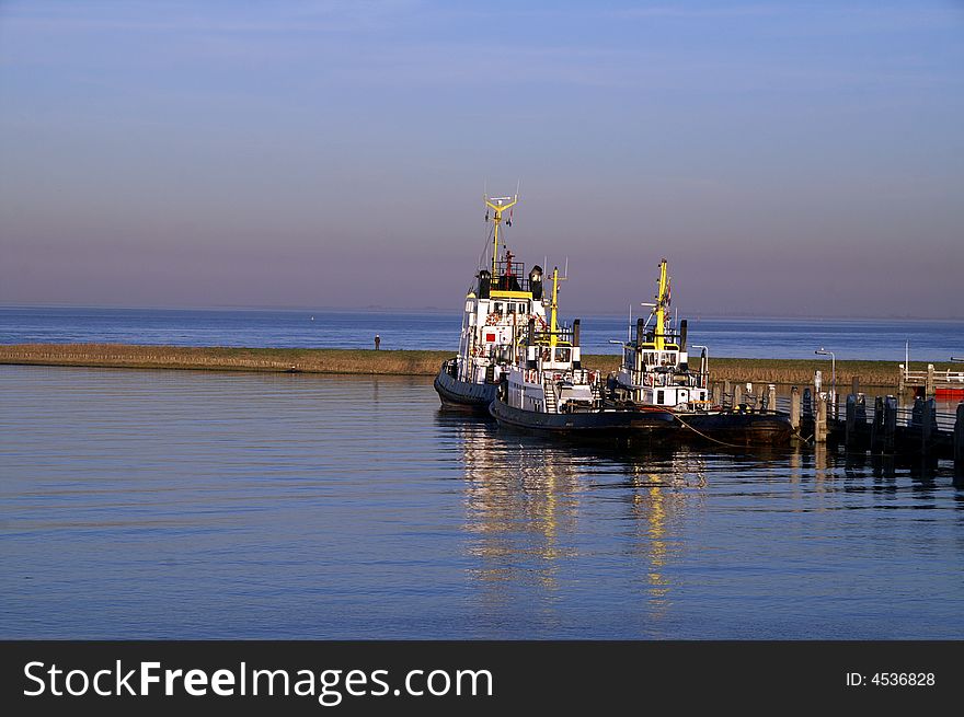Tugboats tied to pier on water against blue sky. Tugboats tied to pier on water against blue sky
