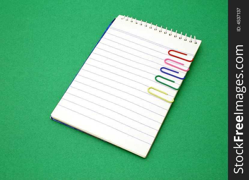 Open notebook with several paper clips over a green surface. Open notebook with several paper clips over a green surface