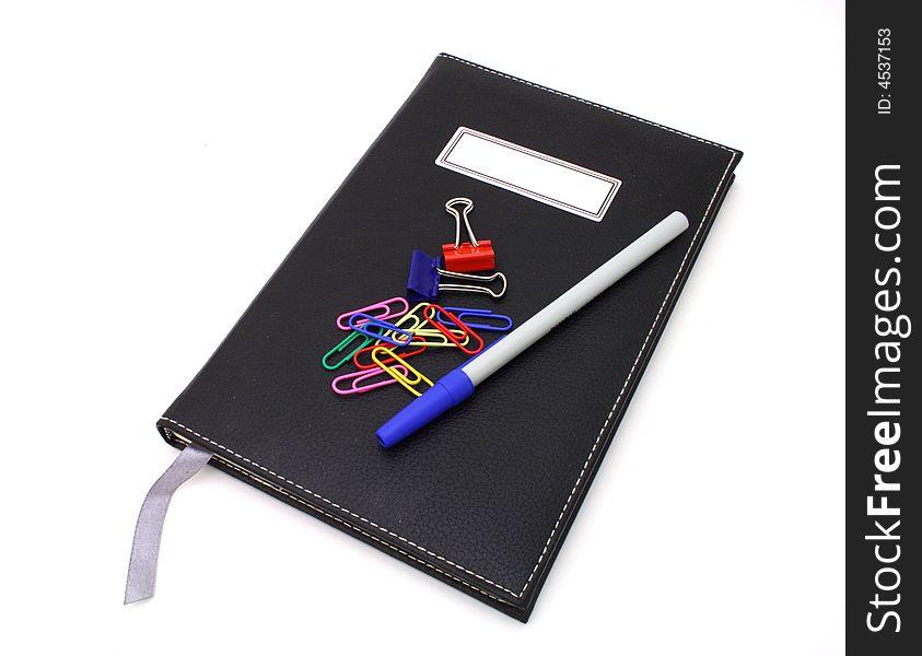 Pen and paper clips over a black journal in a white surface. Pen and paper clips over a black journal in a white surface