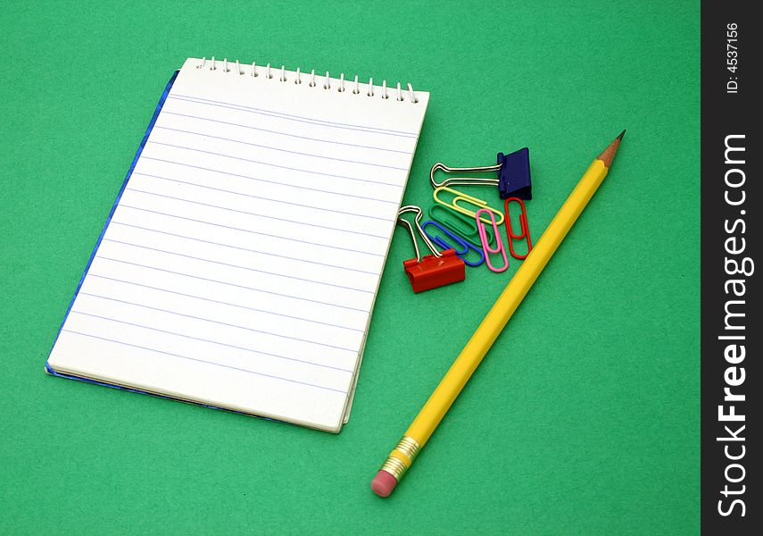 Yellow pen and paper clips besides an open notebook on a green surface. Yellow pen and paper clips besides an open notebook on a green surface