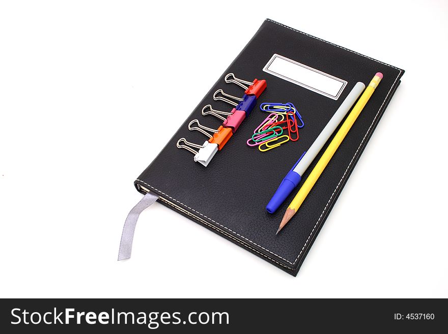 Pen and paper clips over a black journal in a white surface. Pen and paper clips over a black journal in a white surface