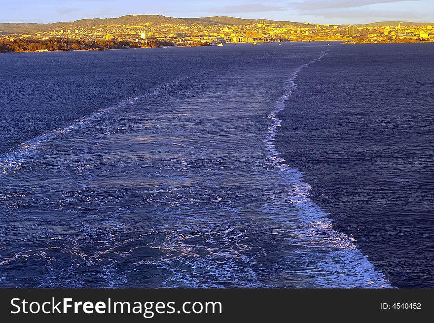 A view of a ships wake and the receding shoreline of Oslo, Norway, as a ship travels out over the water of the Oslo-fjord. A view of a ships wake and the receding shoreline of Oslo, Norway, as a ship travels out over the water of the Oslo-fjord.