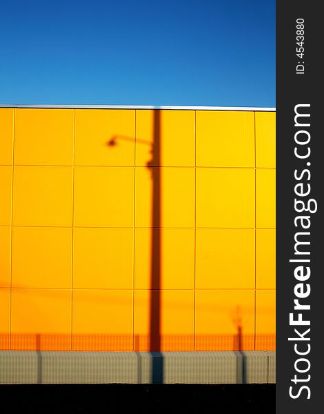 Urban landscape: modern yellow wall with lampost shadow