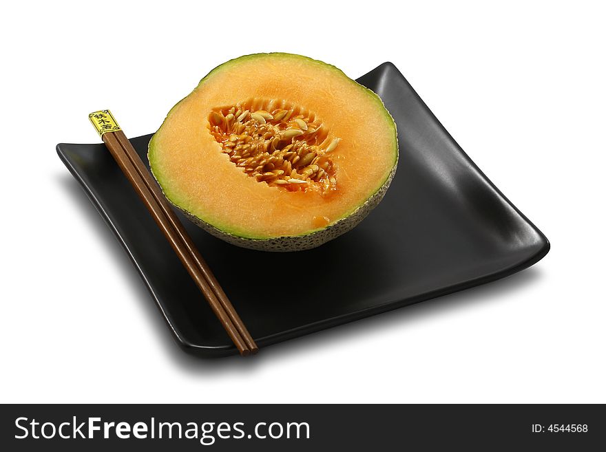Fresh, ripe melon served on stylish, black plate with chopsticks, on white, isolated. Fresh, ripe melon served on stylish, black plate with chopsticks, on white, isolated