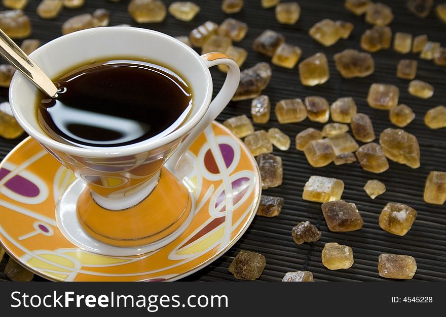 Colorful cup of coffee full of black coffee surrounded by cubes of crystallized brown sugar. Room for copy on the right.