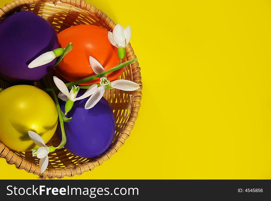 Easter basket with snowdrops and eggs on a yellow background