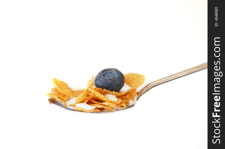 Spoon full of corn flakes with a blueberry isolated on a white background. Spoon full of corn flakes with a blueberry isolated on a white background.