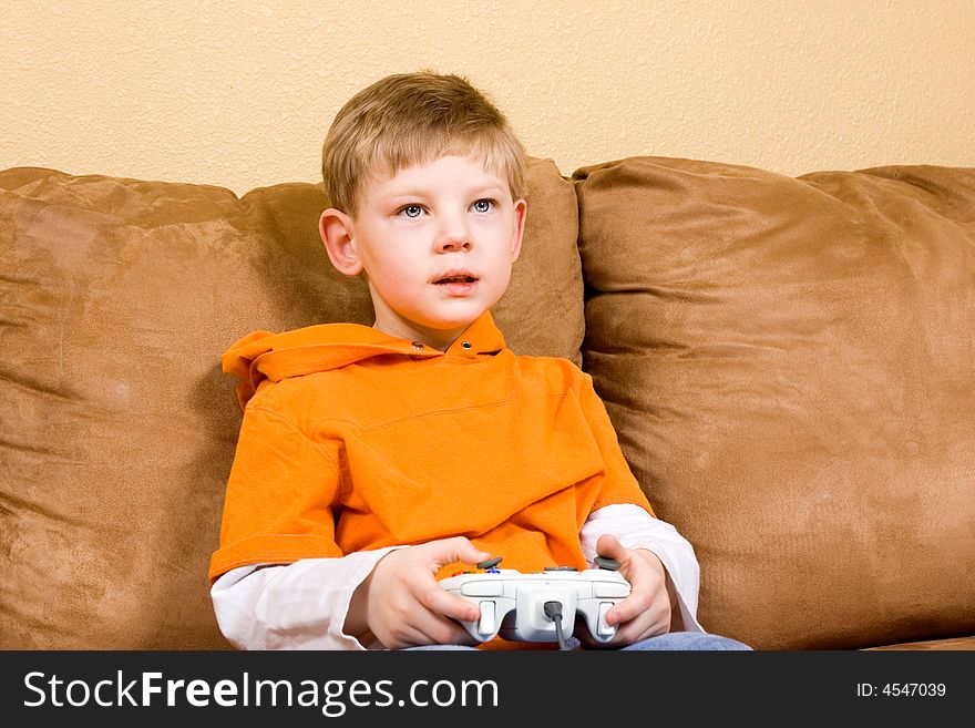 Here is a photo of a young boy sitting on a couch playing a video game. Here is a photo of a young boy sitting on a couch playing a video game.