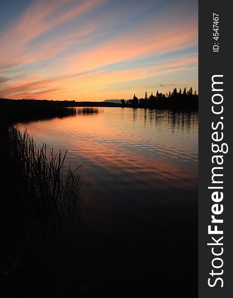 Sunset over a calm lake with a silhouetted forest and shore. Sunset over a calm lake with a silhouetted forest and shore