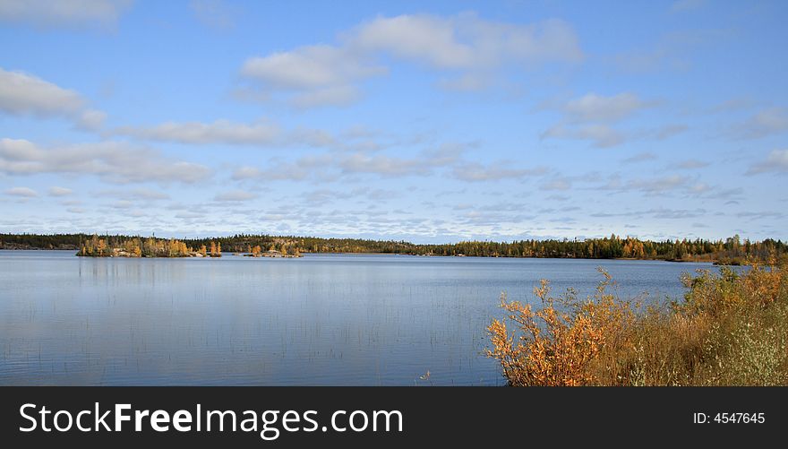 Landscape of a forest reflection in a calm Autumn lake with big blue sky. Landscape of a forest reflection in a calm Autumn lake with big blue sky