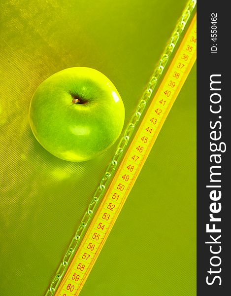 The green apple lays on a gold background with tape measure and a chain. The green apple lays on a gold background with tape measure and a chain