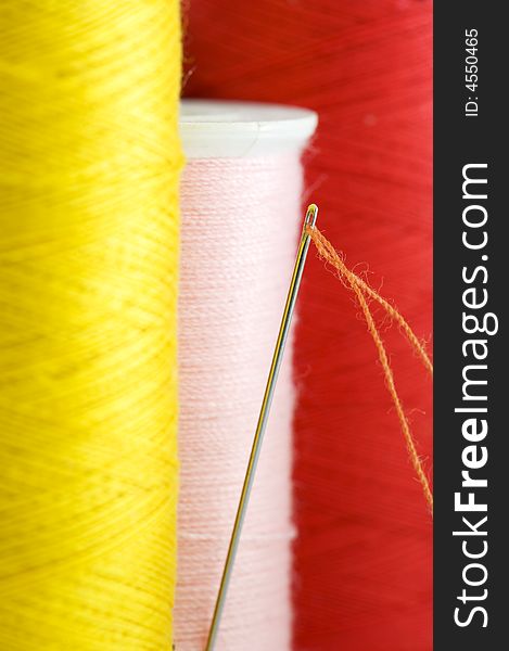 Threads in yellow, pink and red close up. Focus on needle with orange thread.