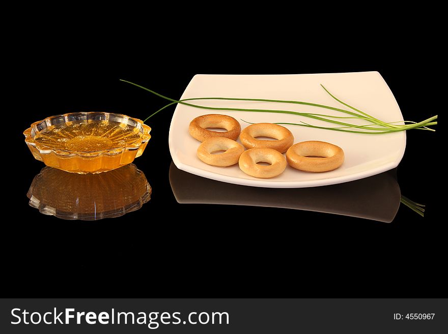 Cut-glass ware with honey and white plate with bagels isolated over black glass. Cut-glass ware with honey and white plate with bagels isolated over black glass