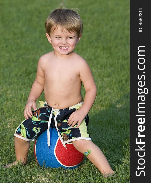 Young boy sitting on a very large blue and red tennis ball. Young boy sitting on a very large blue and red tennis ball
