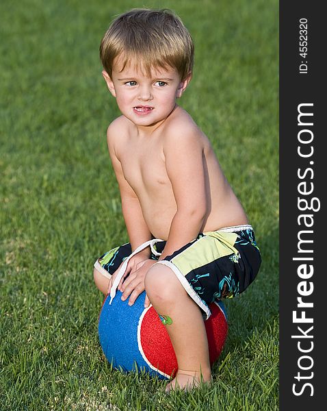 Young boy sitting on a very large blue and red tennis ball. Young boy sitting on a very large blue and red tennis ball