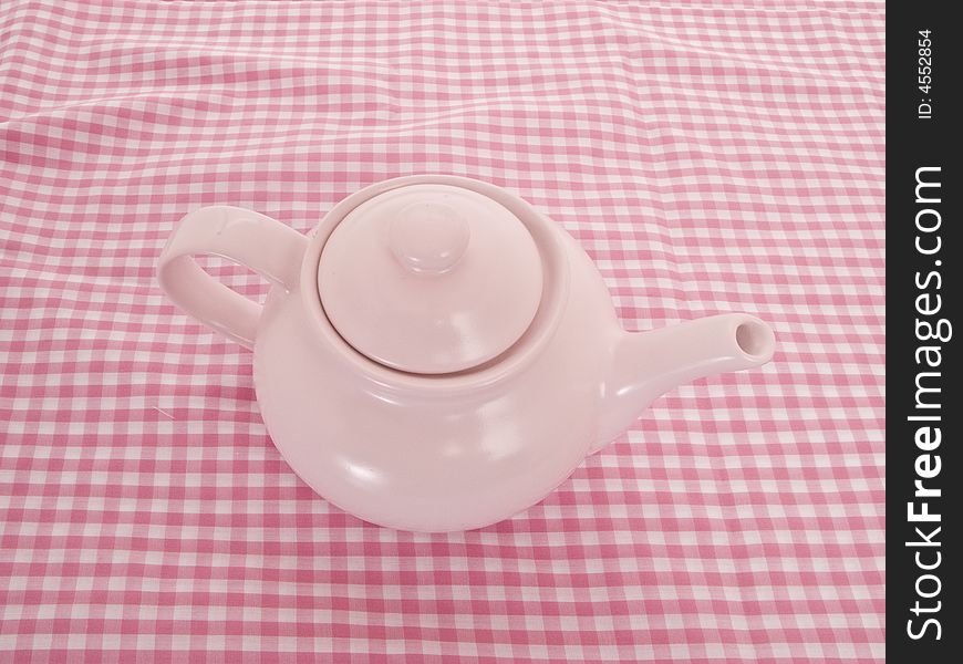 PInk tea pot on a pink picnic table cloth.  Camera angle is from above. PInk tea pot on a pink picnic table cloth.  Camera angle is from above.