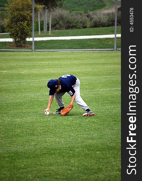 A boy on the outfield retrieving a baseball. A boy on the outfield retrieving a baseball