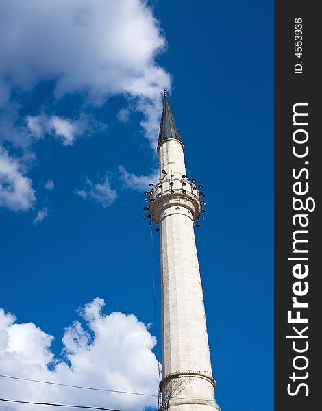 Single minaret of the mosque under the blue and cloudy sky